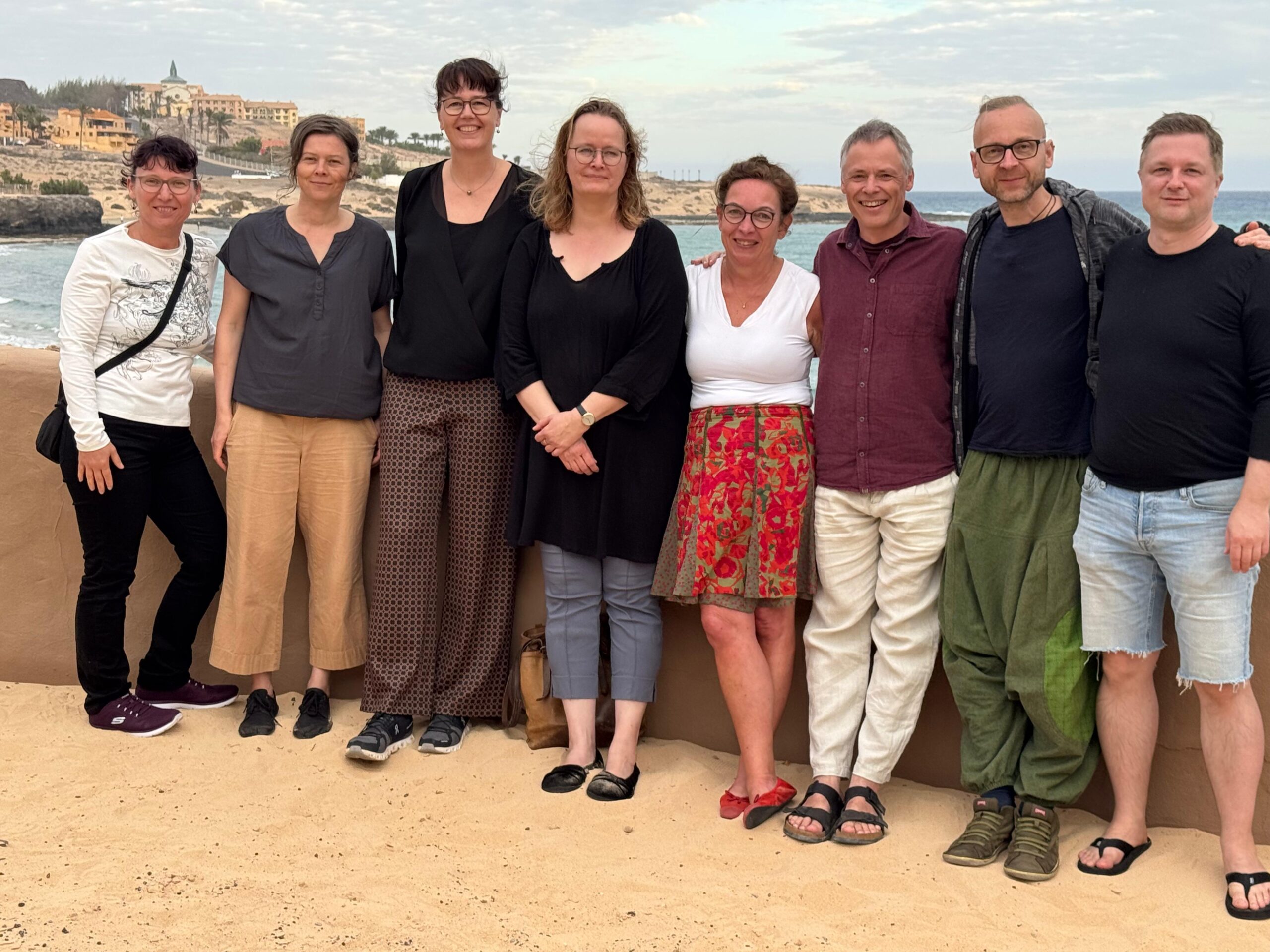 8 Menschen (Teilnehmer der Selbsterfahrungsgruppe auf Fuerteventura) vor dem Hintergrund der Küste an der Costa Calma